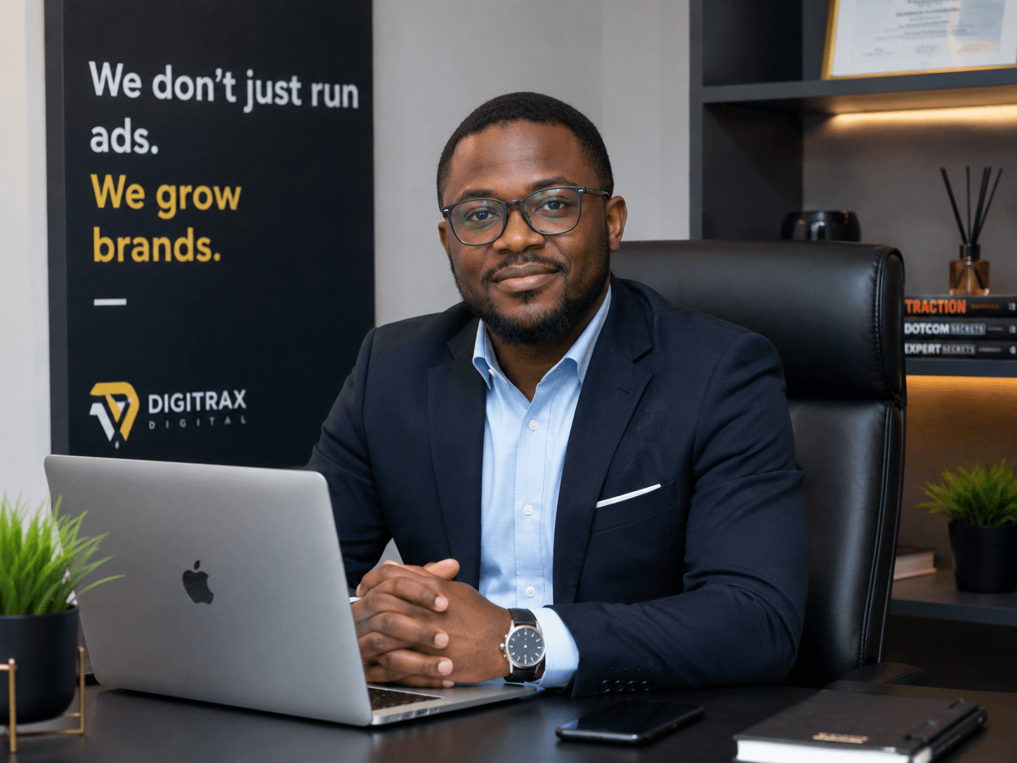 Professional Black man in a blazer and glasses sitting at a desk with a laptop.