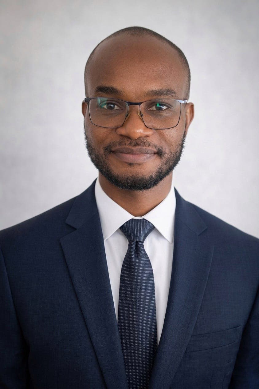 Black man with glasses and a beard wearing a professional navy blue suit and tie.